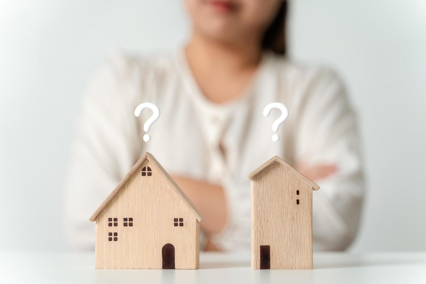 woman is deciding to choose house with Small Wooden House Model with Question Marks, Planning to buy property. Choose what's the best. home loan concepts. photo