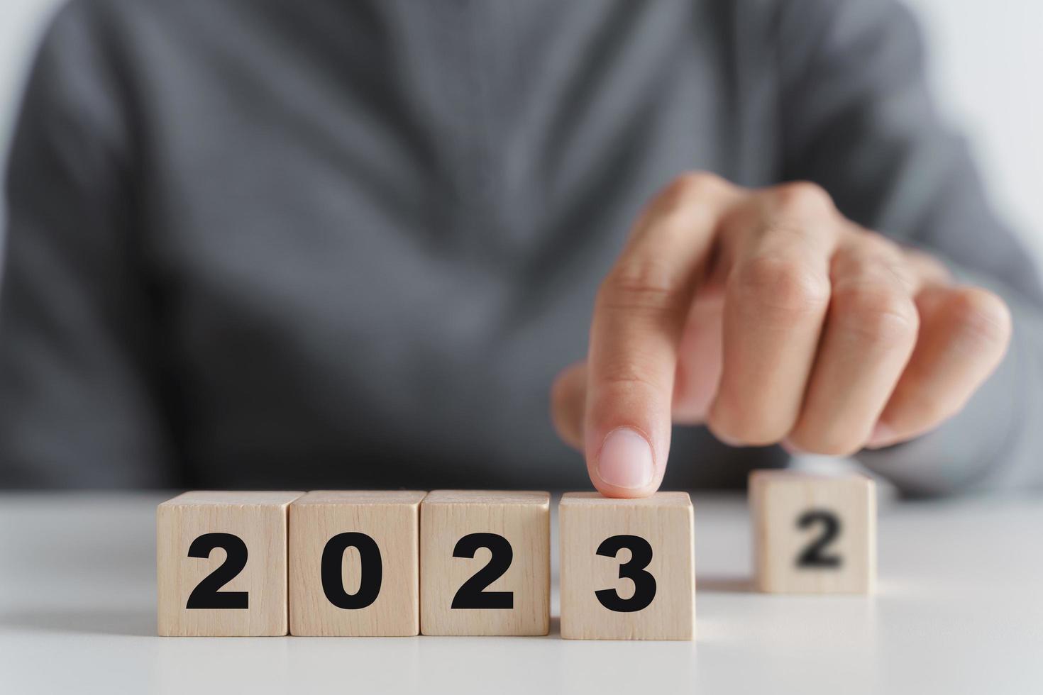 mano de hombre poniendo bloque de cubo de madera para cambiar el año 2022 al año 2023. comienzo del año 2023. concepto de feliz año nuevo. foto