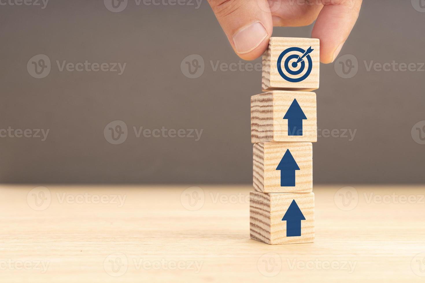 Business goal and objective target concept. Hand holding a cube with target icon and arrows on stacked blocks. Copy space photo