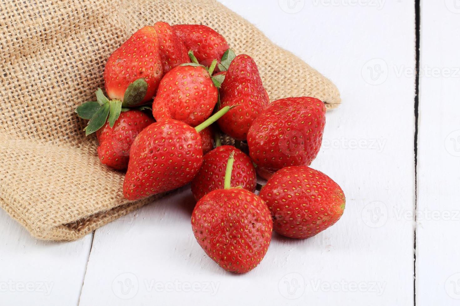 Collection of fresh strawberries on a knitted bag with white painted wooden base photo
