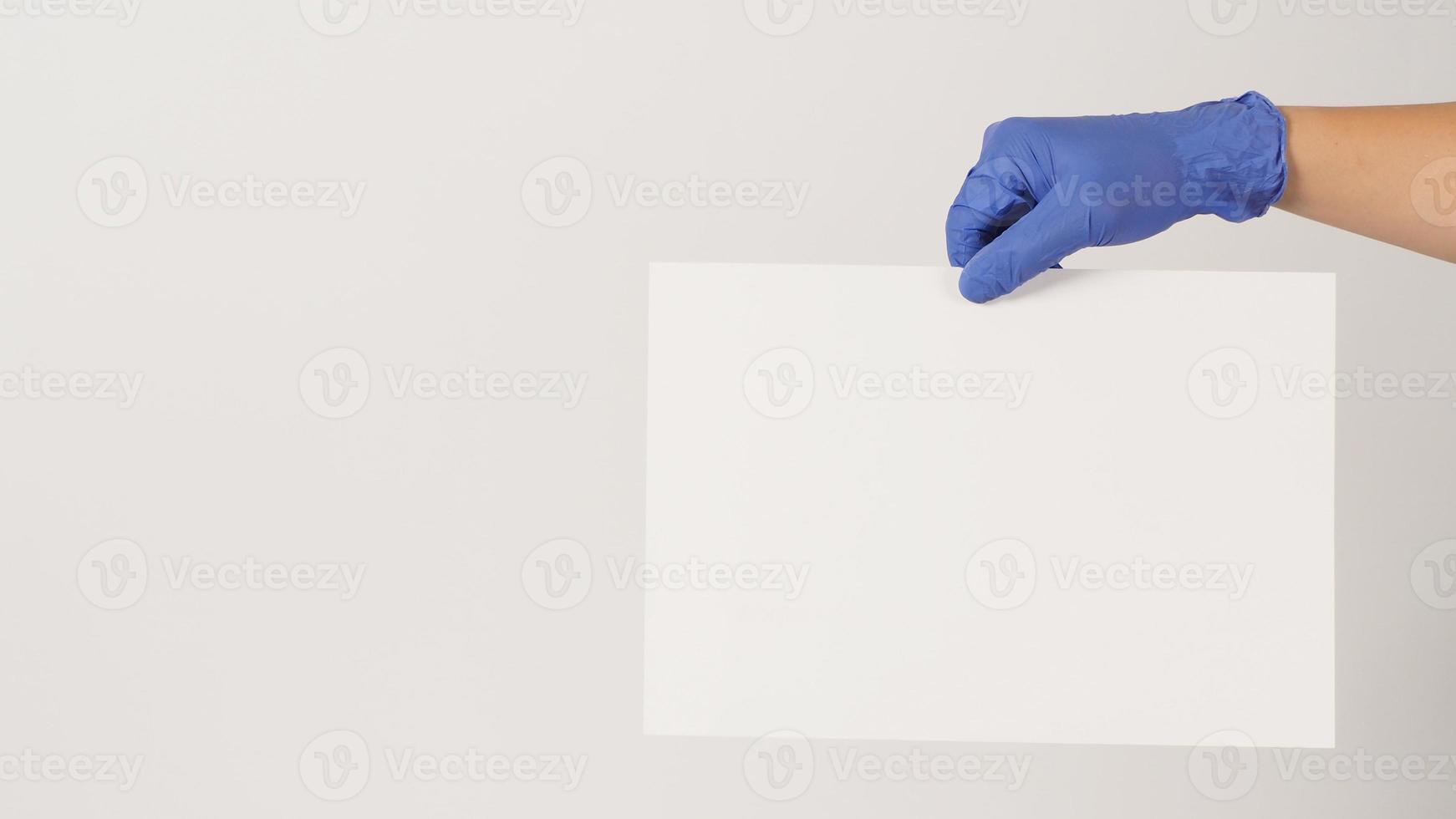 Hand is holding the A4 paper and wear purple latex glove on white background. photo