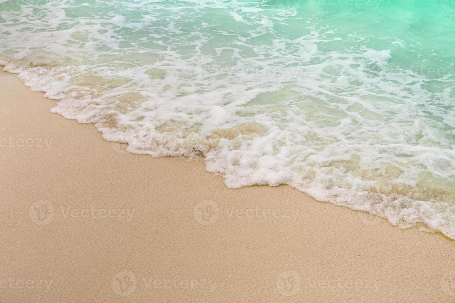 Ola suave y burbuja de mar de mar azul en la playa de arena foto