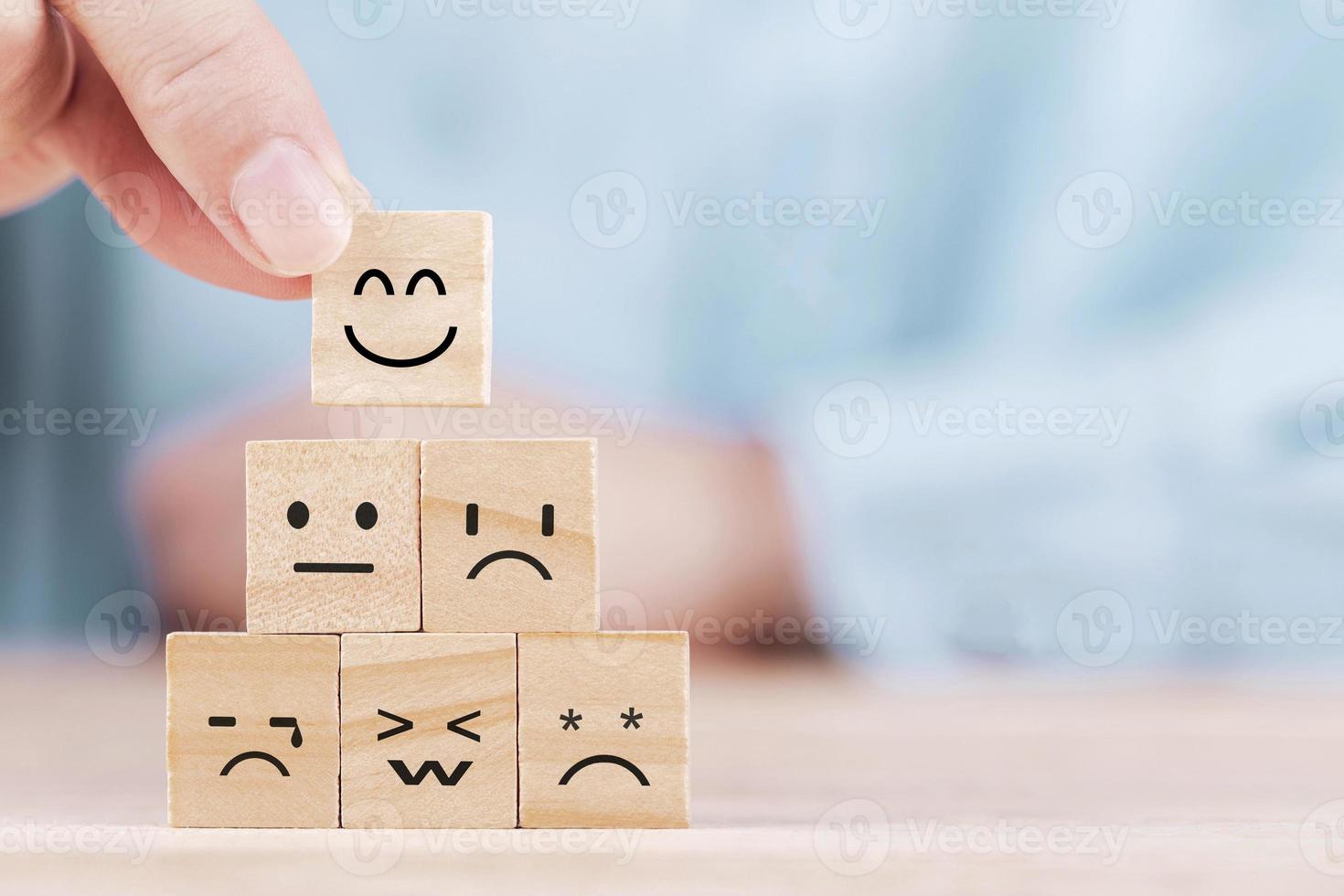 el hombre de negocios elige un icono de emoticono de sonrisa que se enfrenta a un símbolo feliz en un bloque de madera, servicios y concepto de encuesta de satisfacción del cliente foto