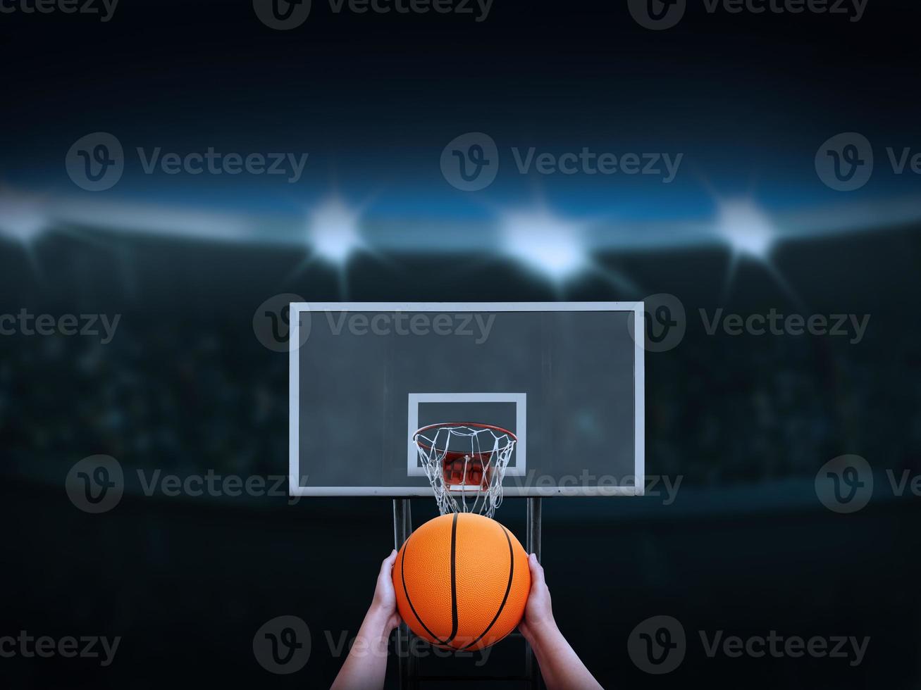 Hand holding a basketball about to shoot it into the basketball backboard There is an amphitheater in the background. photo