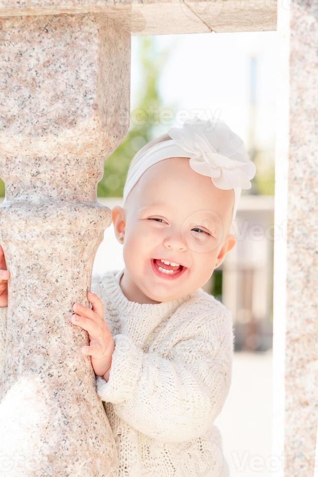 portrait of a smiling little blonde girl with short hair, with a flower headband. Cute and smiling little girl on the street. photo