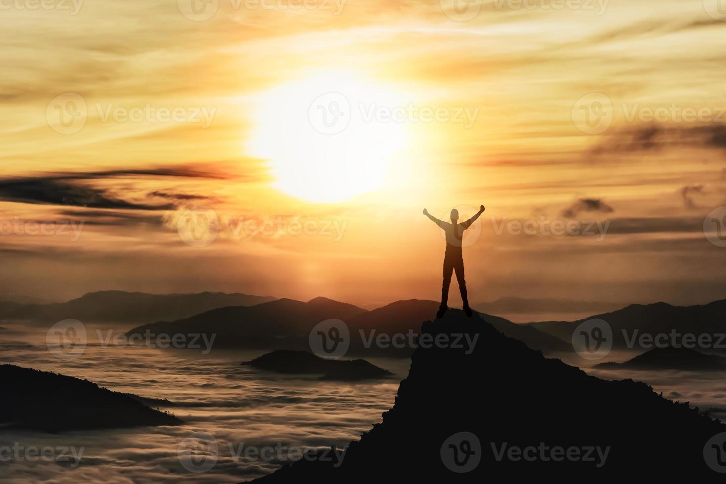 Silhouette man standing and raise two hand on peak stone rock in mountain and watching to sunrise fog, mist, sunset, sunlight. Misty valley. Man hike.Person silhouette stand. Mountain nature concept. photo