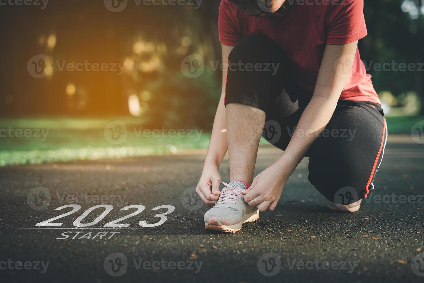 Sport woman runner tie shoelaces start into the new year 2023. Start up of runner woman running on nature race track go to Goal of Success. People running as part of Number 2023. Sport health care. photo