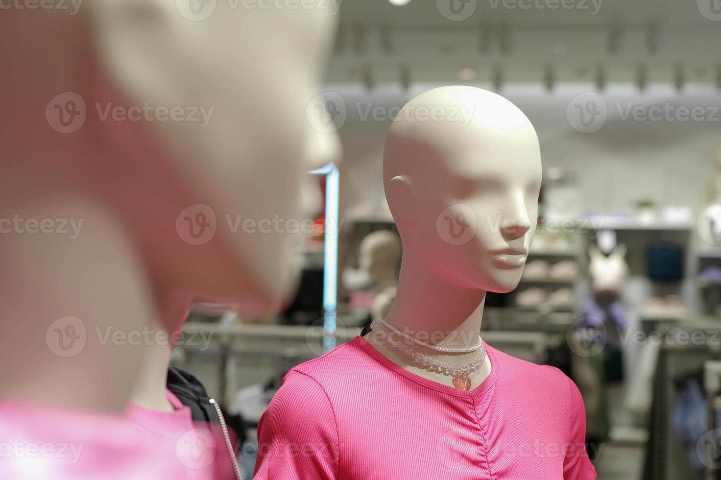 Closeup clear face without hair of female mannequins wearing the childhood clothes design with blurred background of the shop and blurred foreground of another mannequin. photo