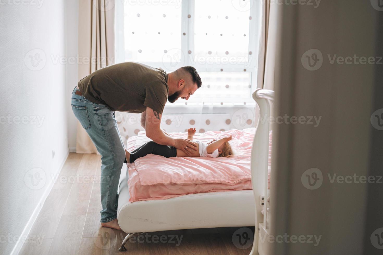 Happy father young man and baby girl little daughter having fun on bed in room at home photo