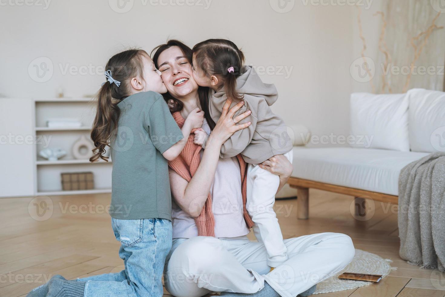 Young happy family with one parent woman mother with two children girls kissing mom in living room at home photo