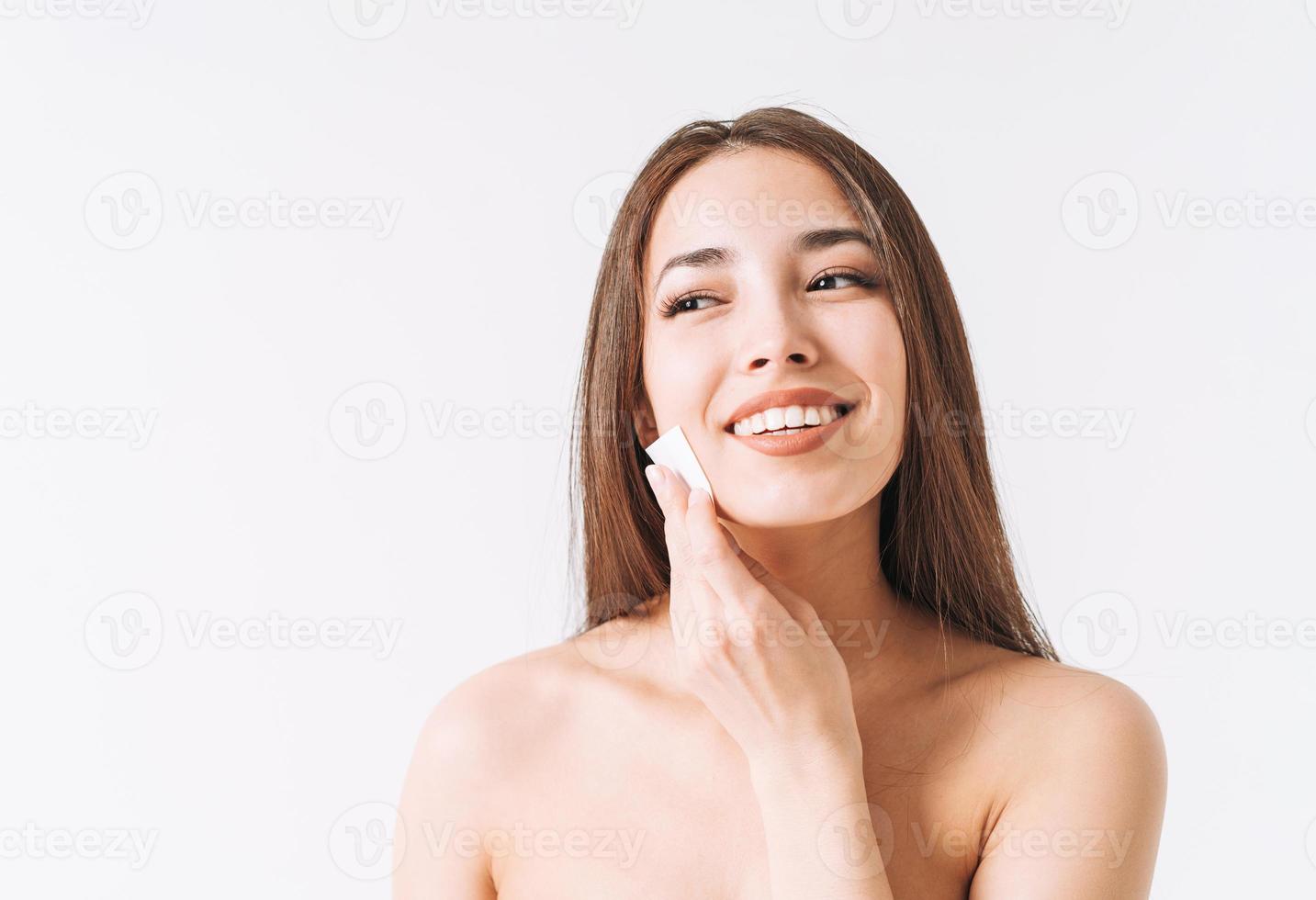 Beauty portrait of happy smiling asian woman with dark long hair with cotton pad on clean fresh skin face and hands on white background isolated, skin cleansing and removing makeup photo