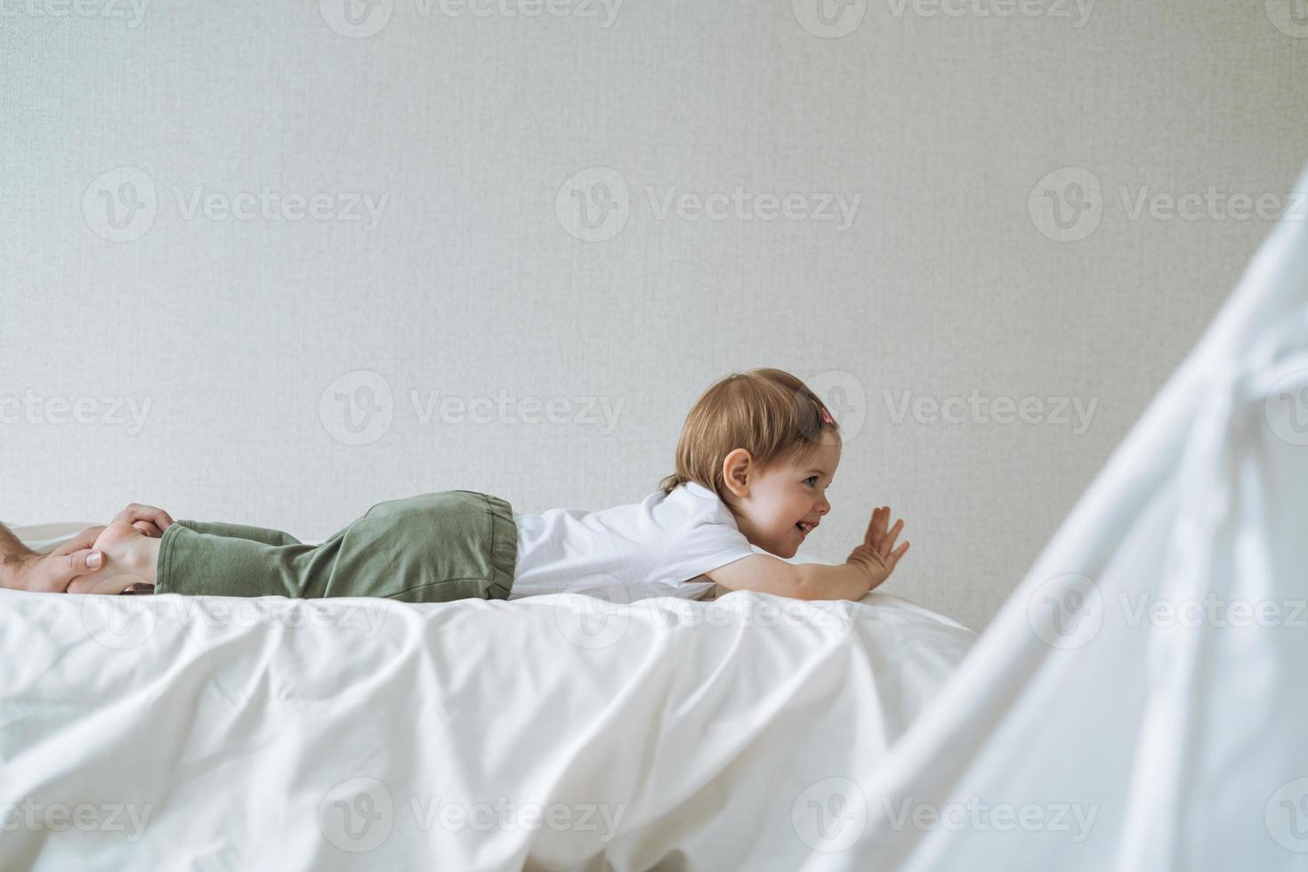 Cute baby girl little daughter having fun with father on bed in children room at home photo