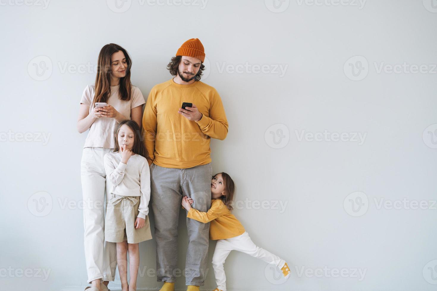 Young happy family with two children girls on gray wall background, parents using mobile phones photo