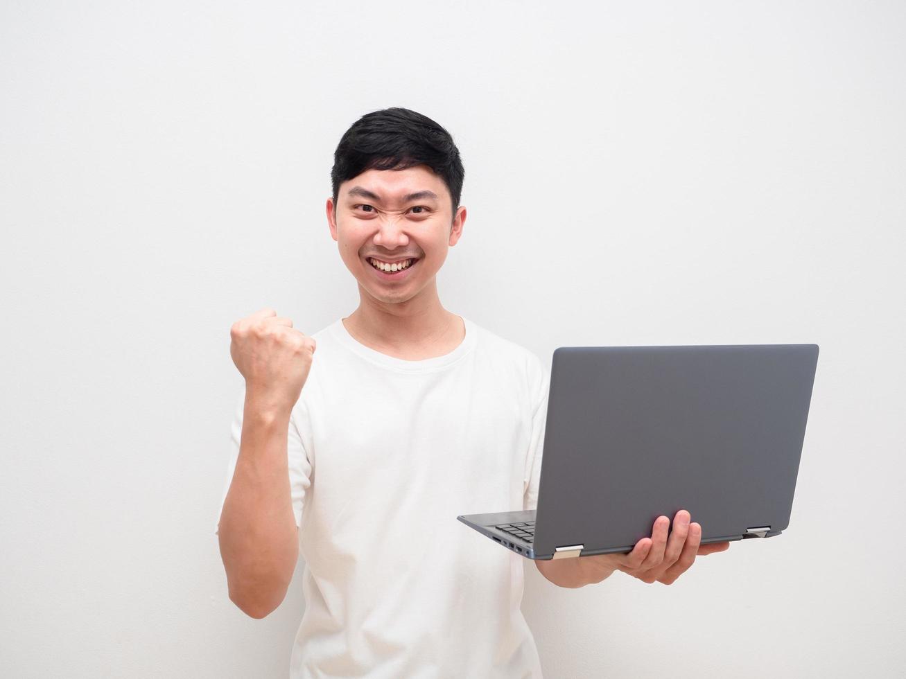 hombre asiático camisa blanca sostenga la computadora portátil en la mano y puño arriba con una sonrisa feliz en su rostro sobre fondo blanco foto