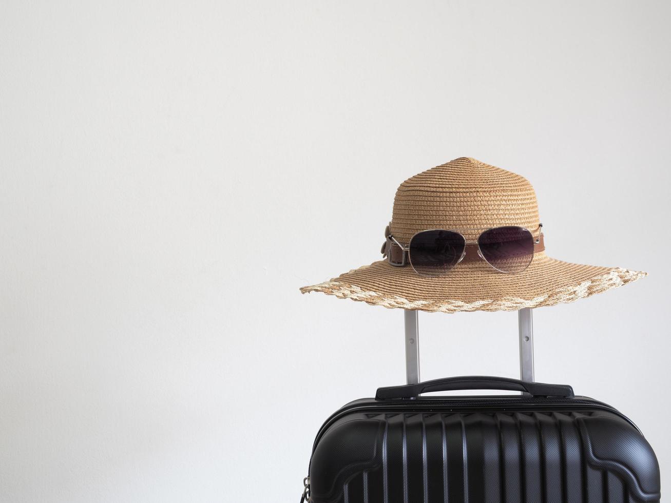 Closeup retro hat with sunglasses above luggage on white isolated space holiday and travel concept photo