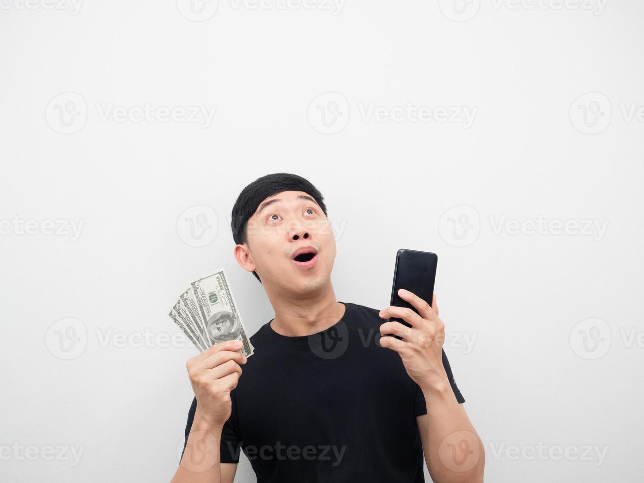 hombre con dinero y teléfono móvil sintiéndose emocionado mirando hacia arriba foto