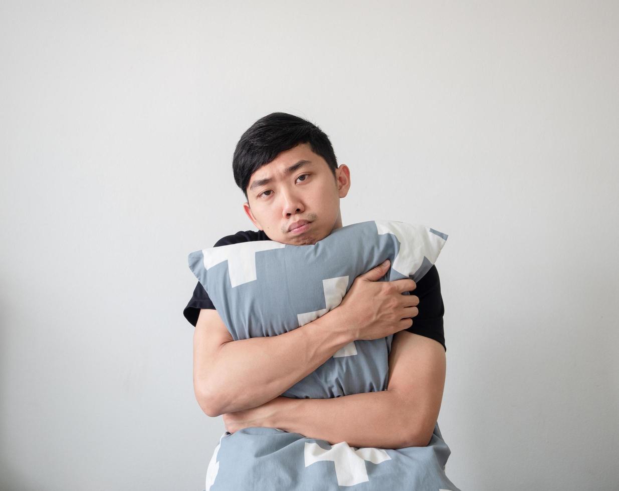 Young man wake up and hugging pillow look at camera bored face on white isolated background photo