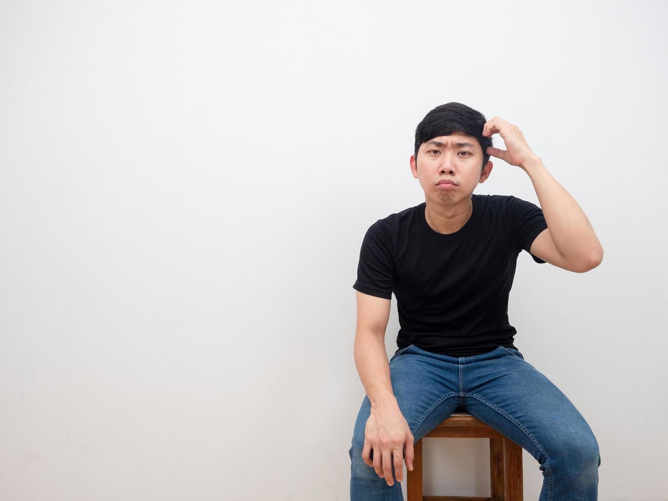 un hombre asiático toca su cabeza sentado en una silla y se siente confuso mirando la cámara con fondo blanco foto