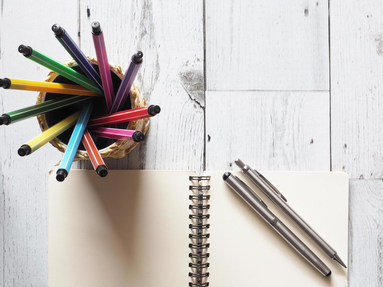 Pen colorful array circular in box with open notebook blank with two silver pen on white wood table and nature light of sun idea concept top view,business and education photo