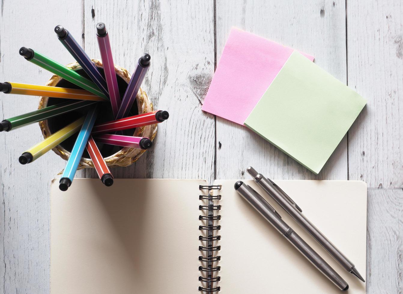 Pen colorful array circular in box with open notebook blank with two silver pen on white wood table with note paper and nature light of sun idea concept top view,business and education photo