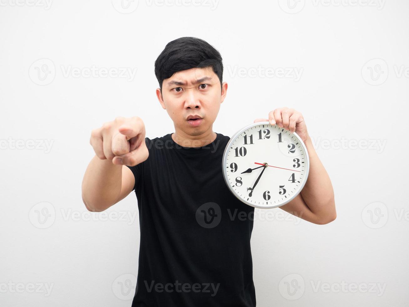 hombre enojado sosteniendo un reloj analógico y apuntándote con el dedo foto