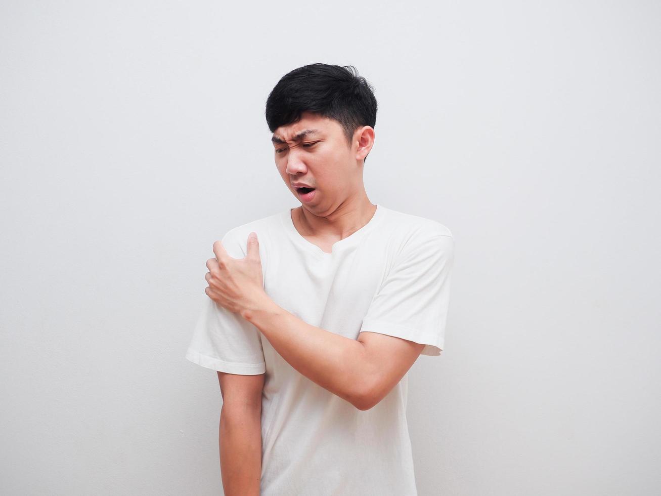el hombre asiático siente dolor en el hombro y toca el hombro con la mano izquierda en el fondo blanco foto