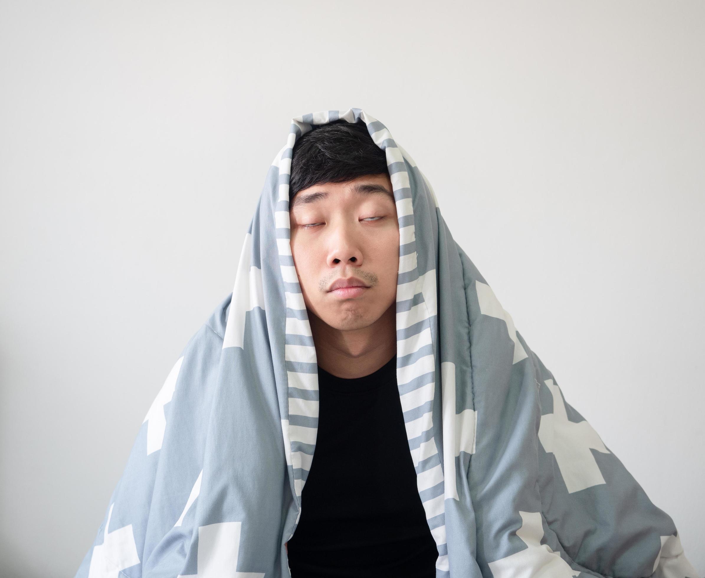 Young man with blanket cover his head wake up and feel sleepy close the