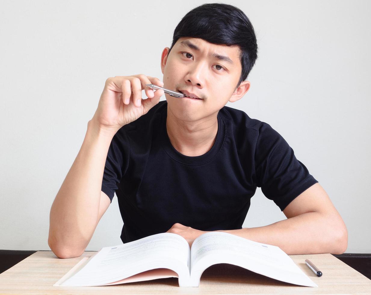Young man with pen think and serious face with the book on the desk look at camera on white isolated,Study book concept photo