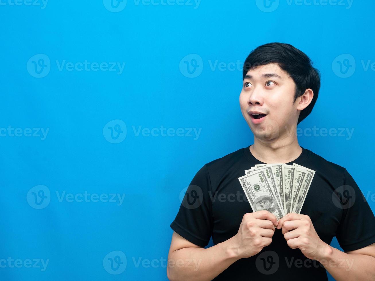 hombre asiático sosteniendo dinero sintiéndose emocionado mirando el espacio de copia fondo azul foto