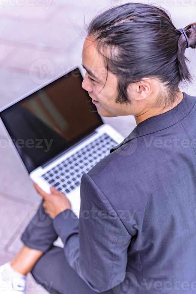 asian male freelancer walking near business center holding phone, smiling reading news, successful businessman photo