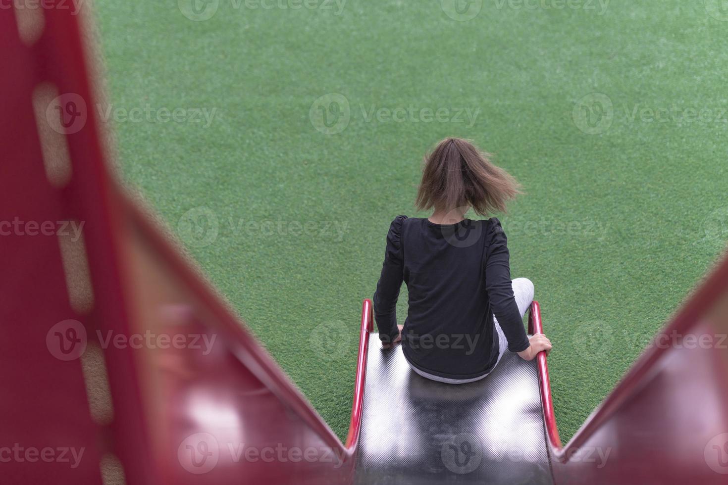 cri du chat, niña autista se desliza en un parque infantil en un parque público. foto