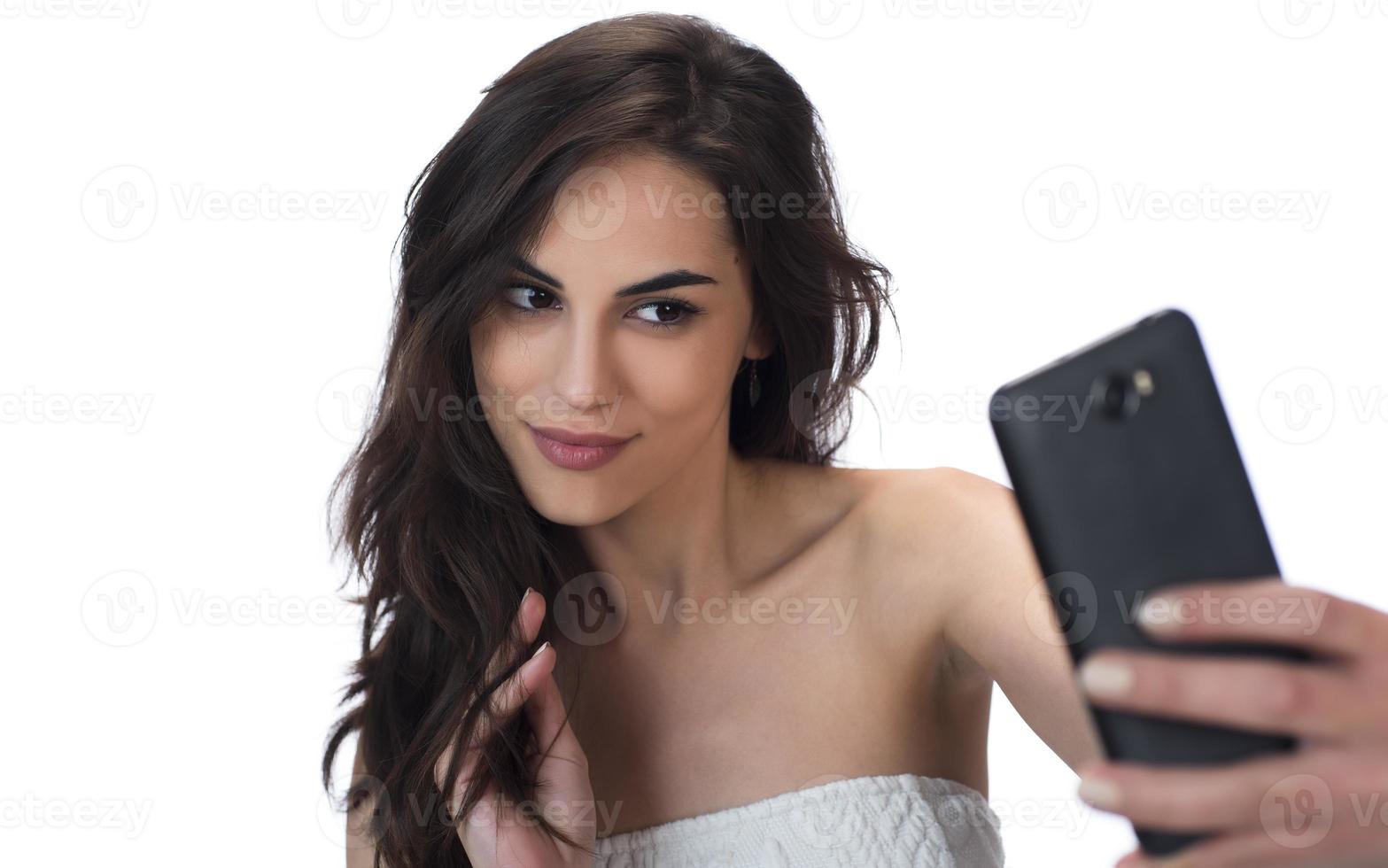 Image of beautiful brunette woman laughing while taking selfie photo on cellphone isolated over white background