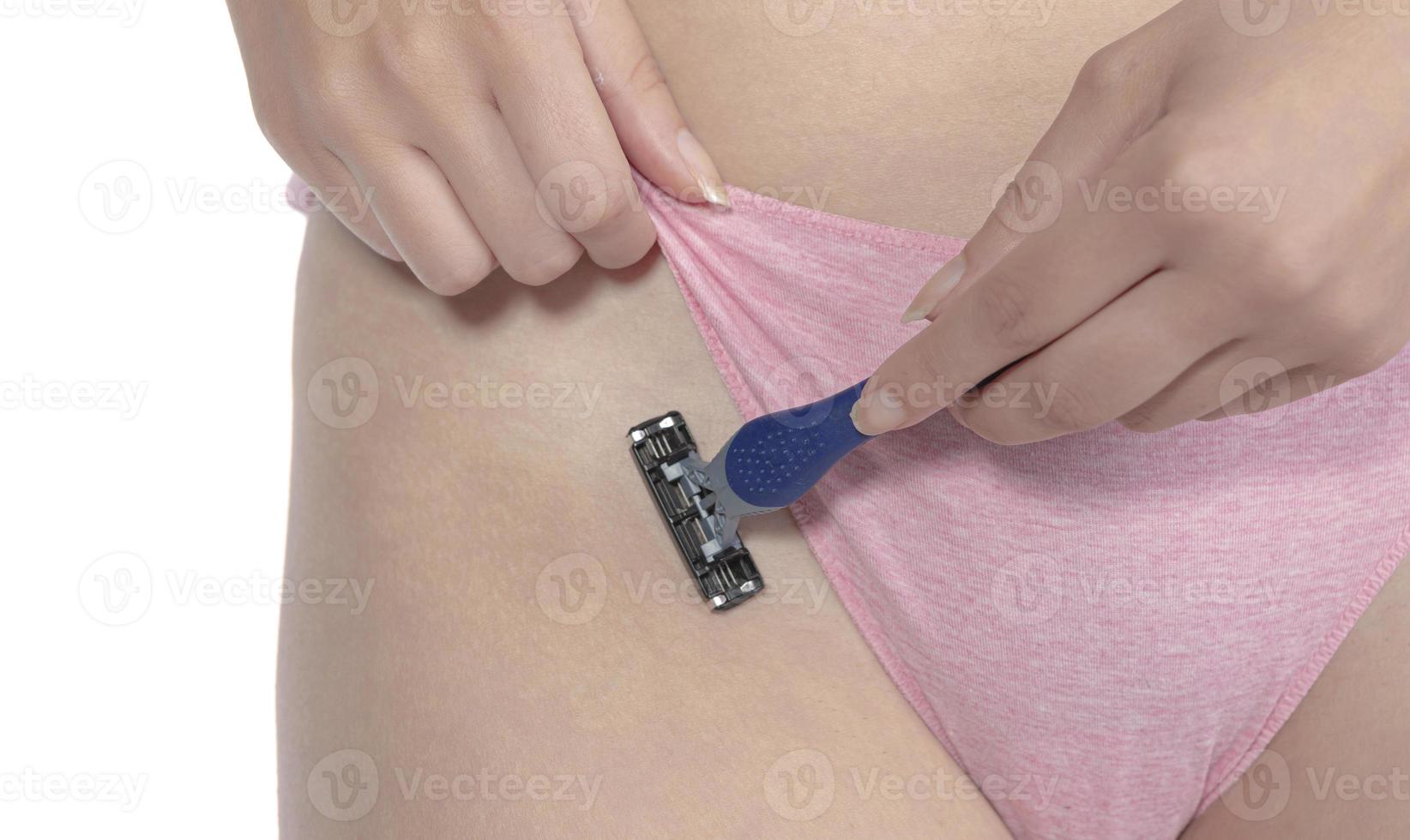 A girl in pink panties shaves her hair in the bikini area with a razor and makes depilation with cream photo