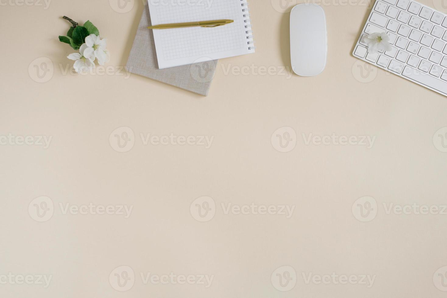 female workspace of a table with delicate flowers of an apple tree, a notebook, a pen, paper clips and a computer on a delicate beige background. flat lay, top view, copy space photo