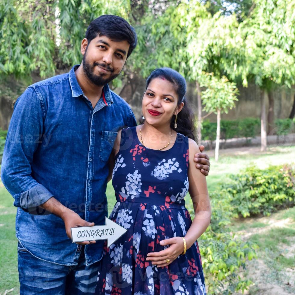 pareja india posando para una sesión de fotos de maternidad. la pareja está posando en un césped con hierba verde y la mujer está faluntando su panza en el jardín lodhi en nueva delhi, india