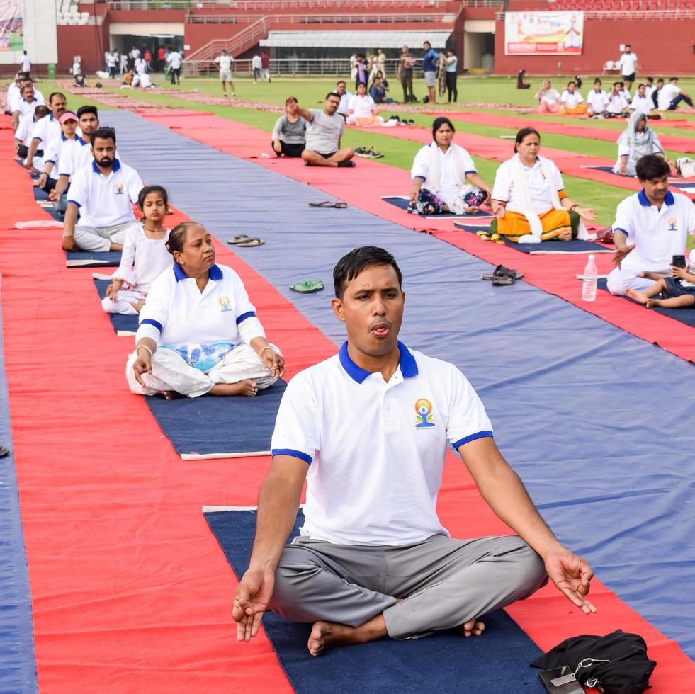 New Delhi, India, June 21 2022 - Group Yoga exercise session for people at Yamuna Sports Complex in Delhi on International Yoga Day, Big group of adults attending yoga class in cricket stadium photo