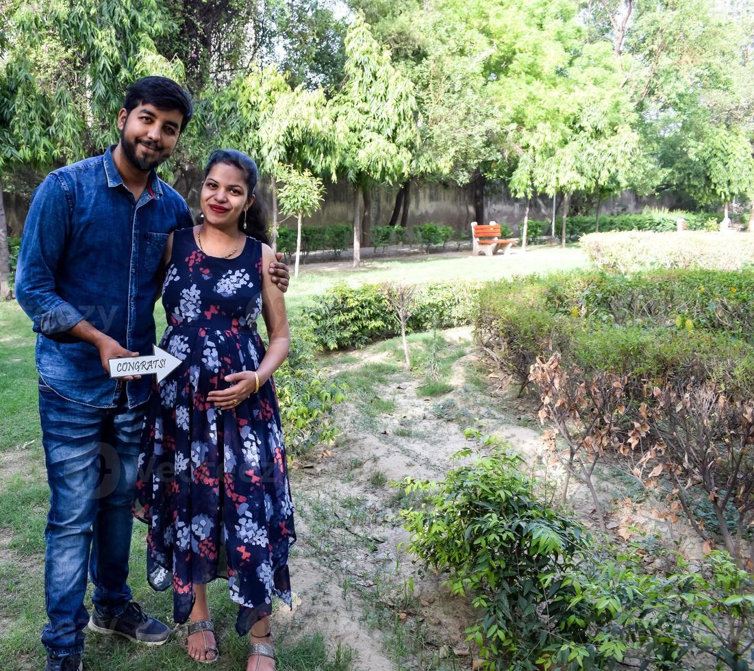 Indian couple posing for maternity baby shoot. The couple is posing in a lawn with green grass and the woman is falunting her baby bump in Lodhi Garden in New Delhi, India photo