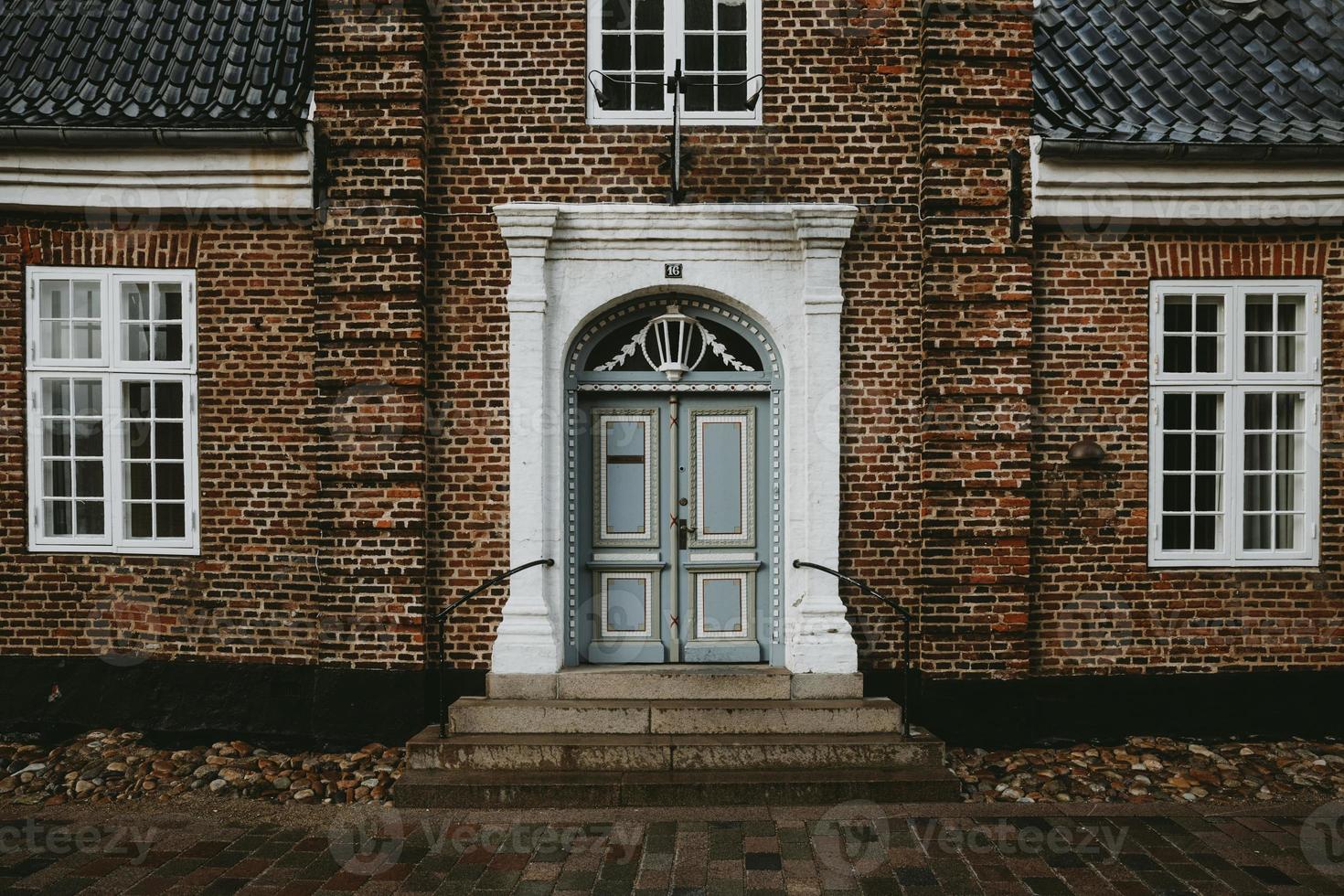 The front view of a old brick house with white windows and entrance with light blue doors in the oldest Denmark town Ribe during the autumn rainy day photo