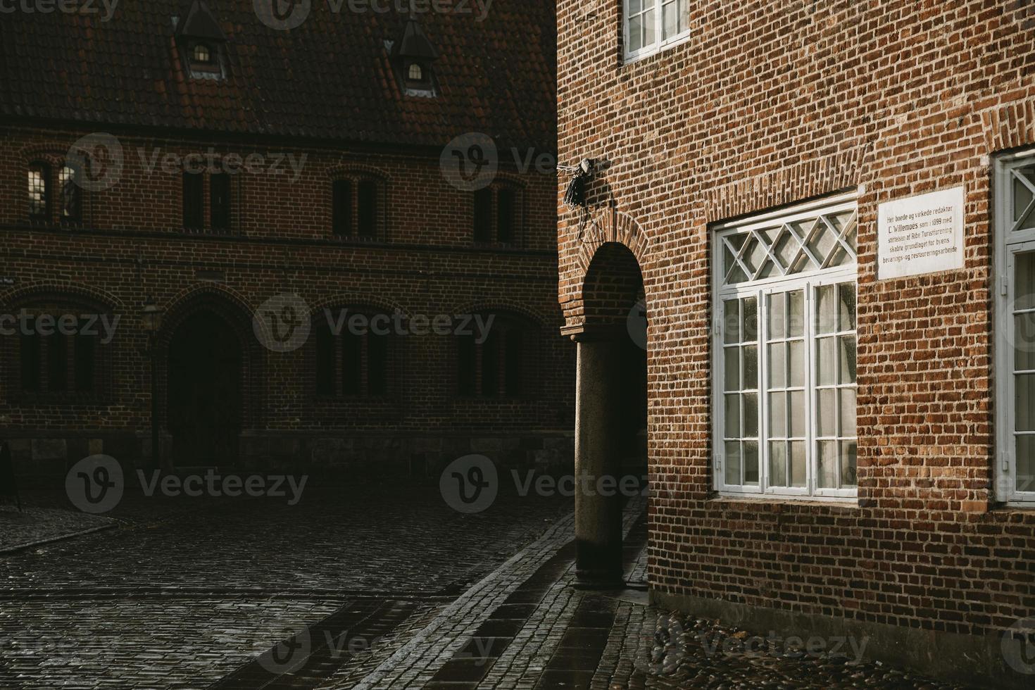 Corner of an old brick house with the underpass supporting by the stone column enlightened with the afternoon sun, with the wet granite road around in the Denmark oldest village Ribe photo