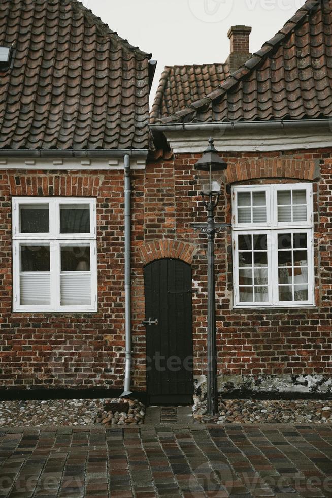 Narrow wooden door between old brick houses with white framed windows with the street lamp and stone road in front of them during the autumn afternoon after the rain in the oldest Denmark village Ribe photo