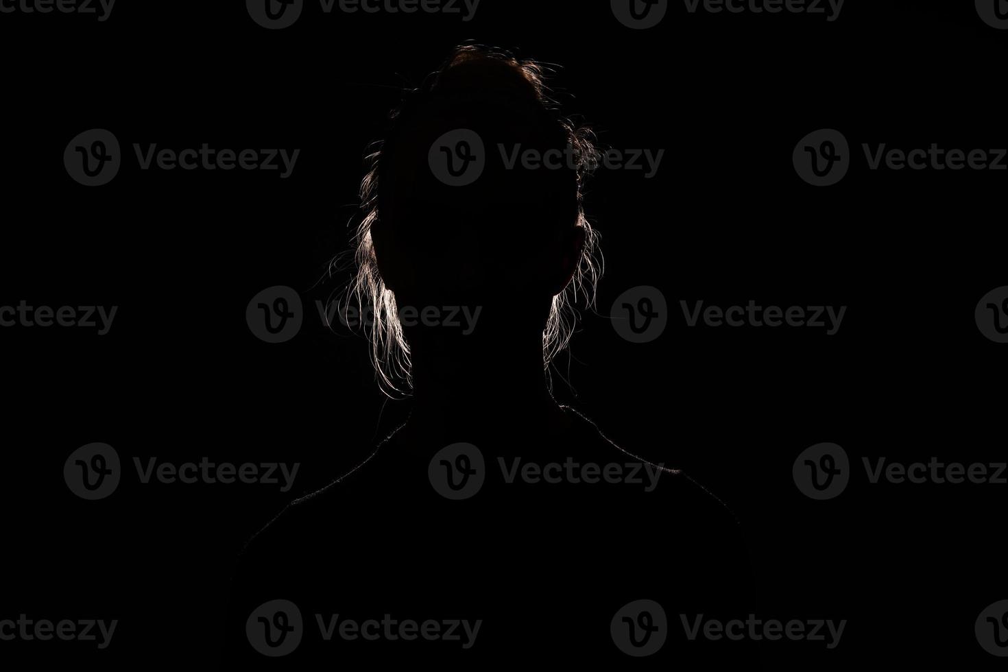 backlit portrait silhouette of unrecognizable woman hiding face and identy in the dark shadow photo