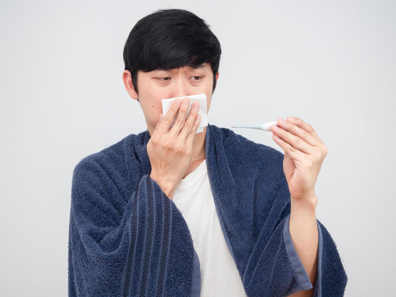 hombre enfermo sosteniendo tejido en su nariz y mirando el termómetro en la mano sintiéndose triste foto