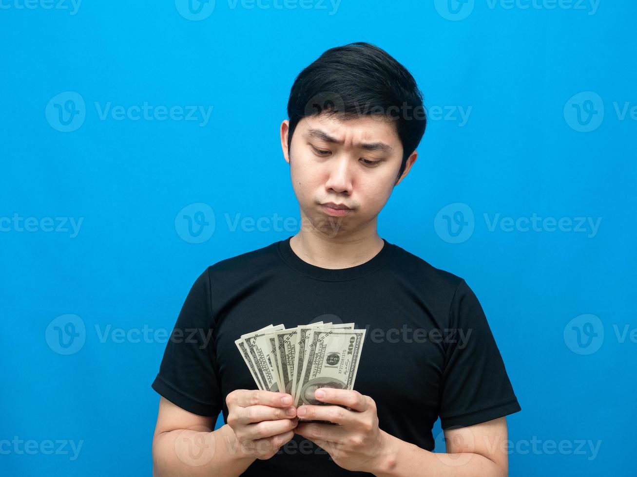 Asian man looking at money in his hand and feeling doubt blue background photo