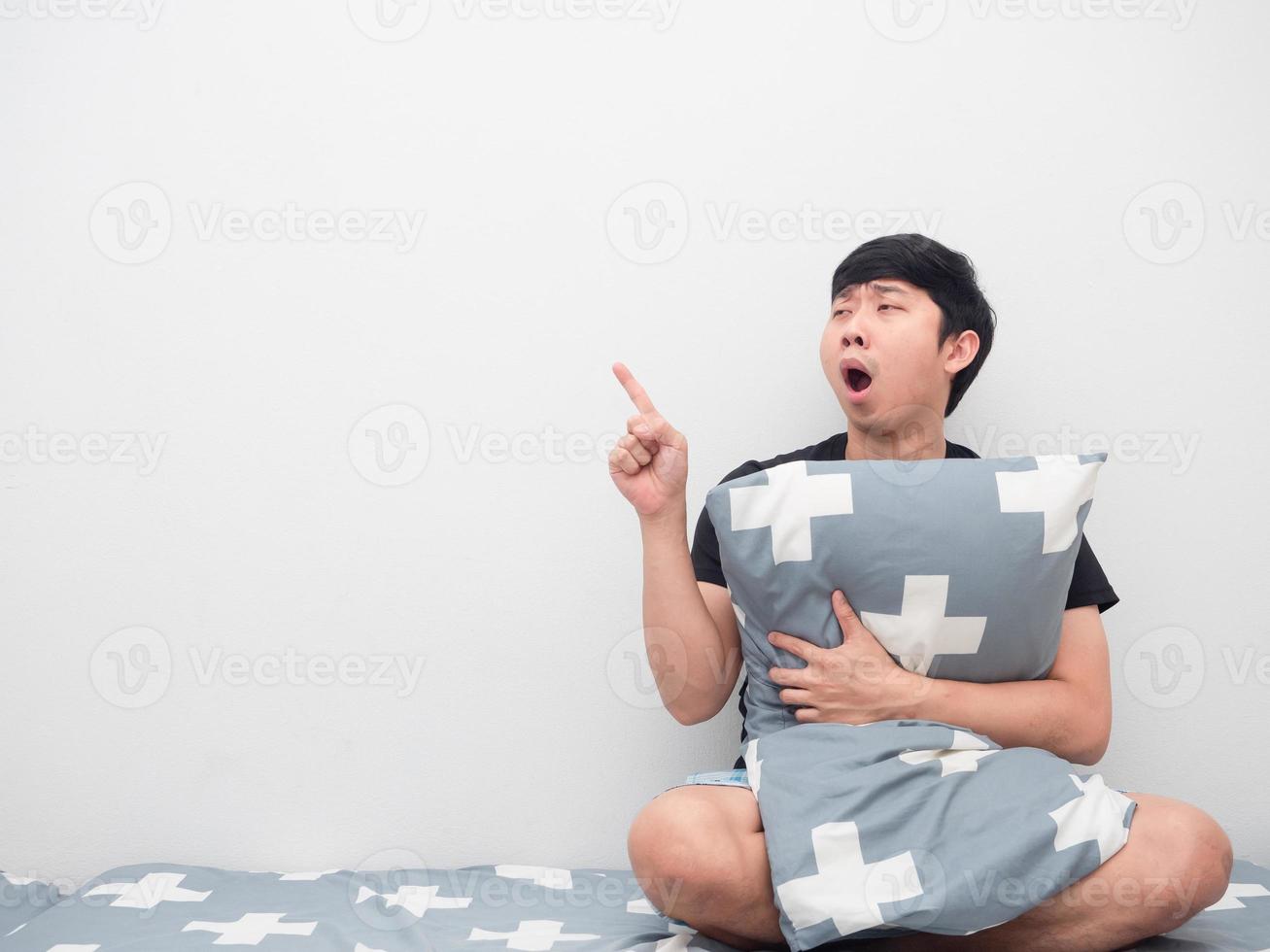 Sleepy man yawn and hug pillow point finer at copy space photo