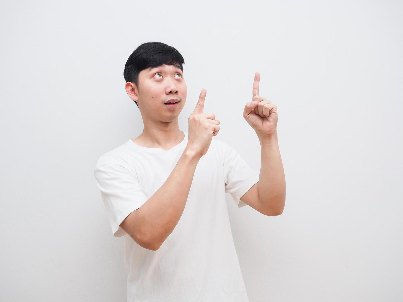 hombre asiático camisa blanca alegre cara apuntar con el dedo doble hacia arriba y mirar hacia arriba sobre fondo blanco foto