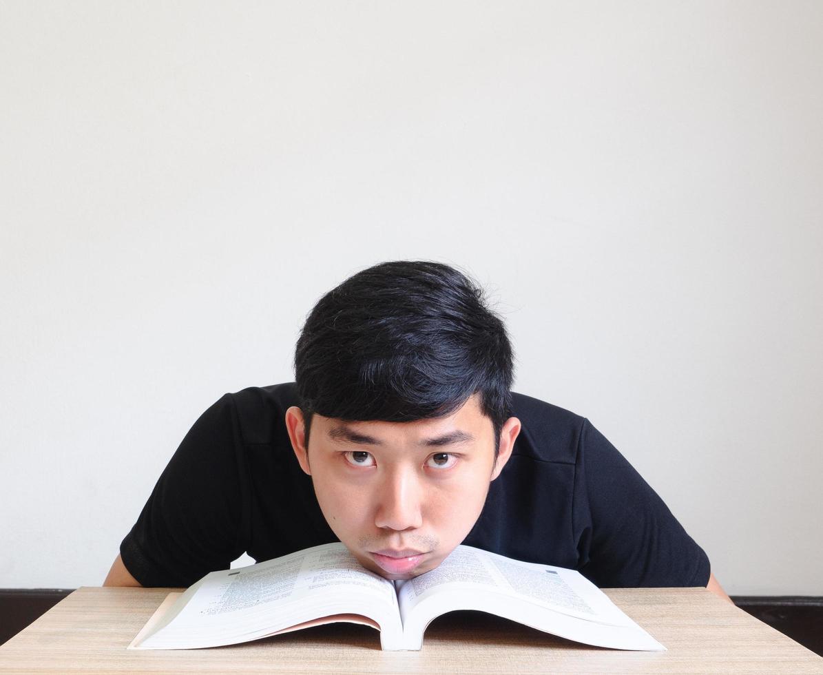 joven asiático aburrido cara con leer el libro siente tristeza en el escritorio mira la cámara aislada, concepto de educación foto