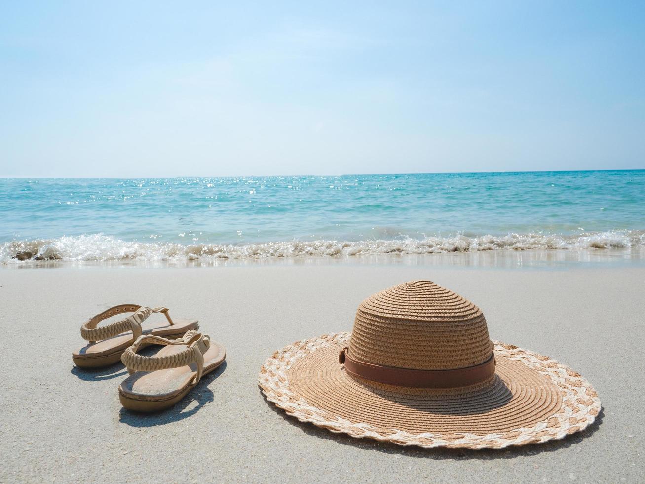 sombrero y zapato de mujer pn la playa y las olas del océano paisaje de cielo azul foto