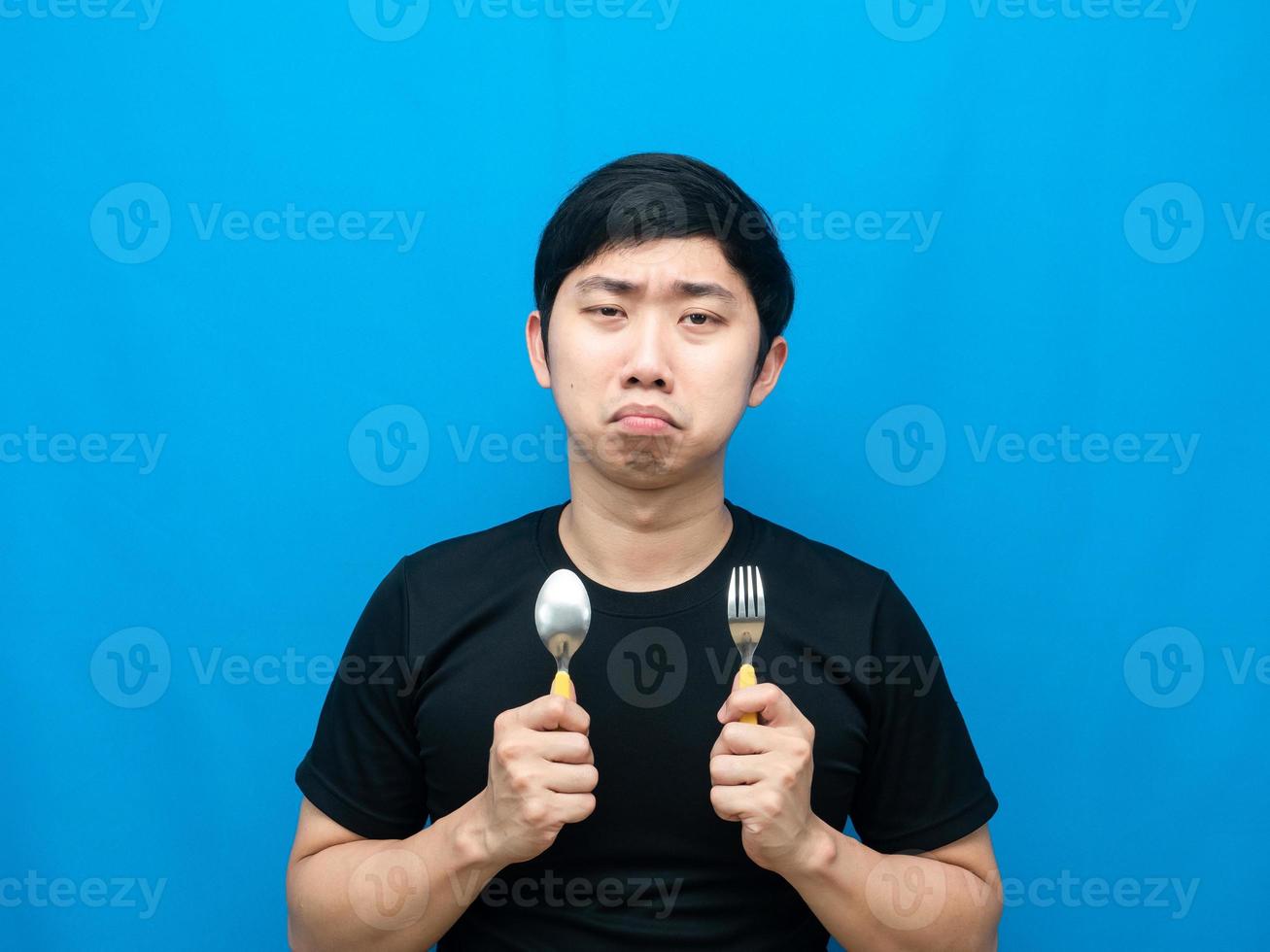 hombre hambriento sosteniendo cubiertos sintiendo tristeza emoción fondo azul foto