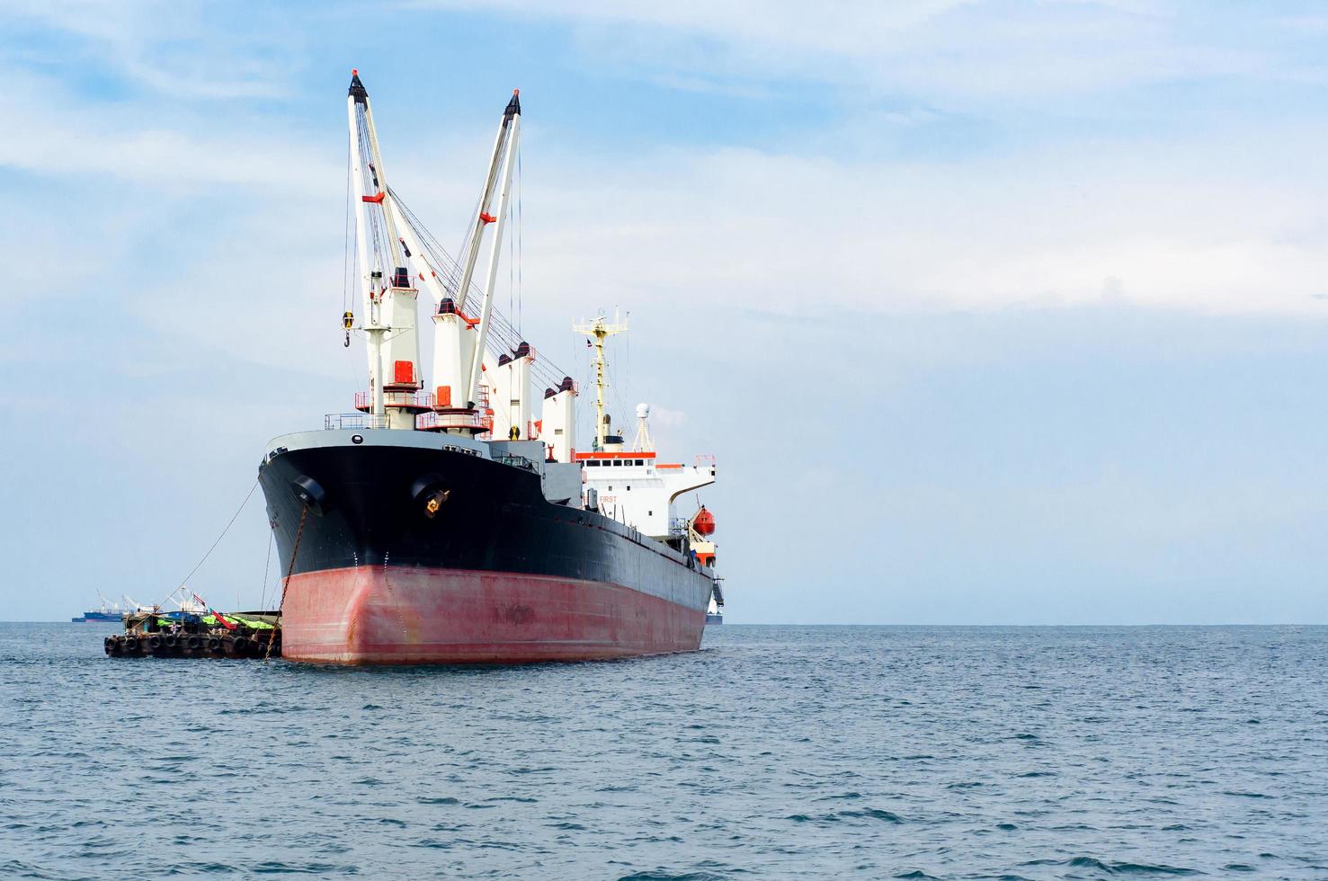 Big crane in the cargo ship unloading in the blue ocean and sky and mountain background landscape,Logistic boat in the industrial sea concept space photo