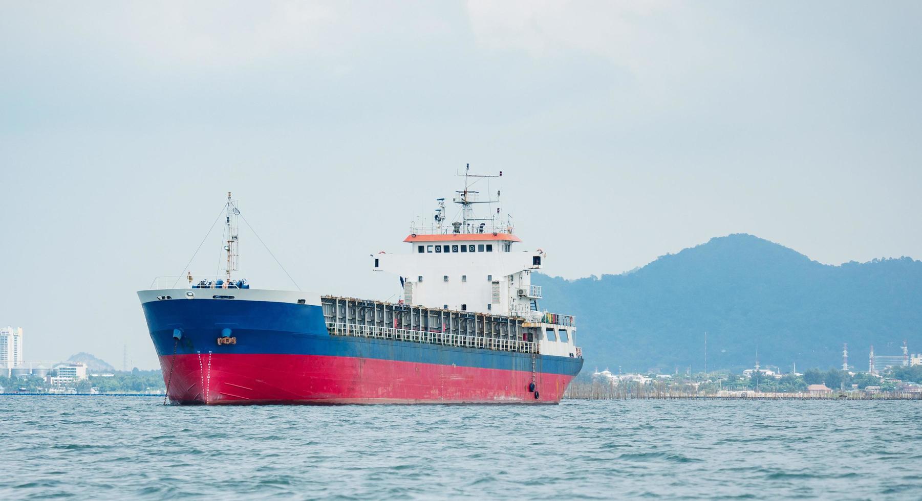 buque de carga en el océano con el fondo de la isla y la montaña, buque de transporte en el frente marítimo del muelle y la isla con el cielo azul foto